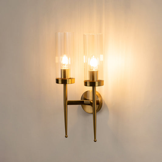 Modern brass wall light with dual clear glass shades creating warm luxury interior lighting decor.