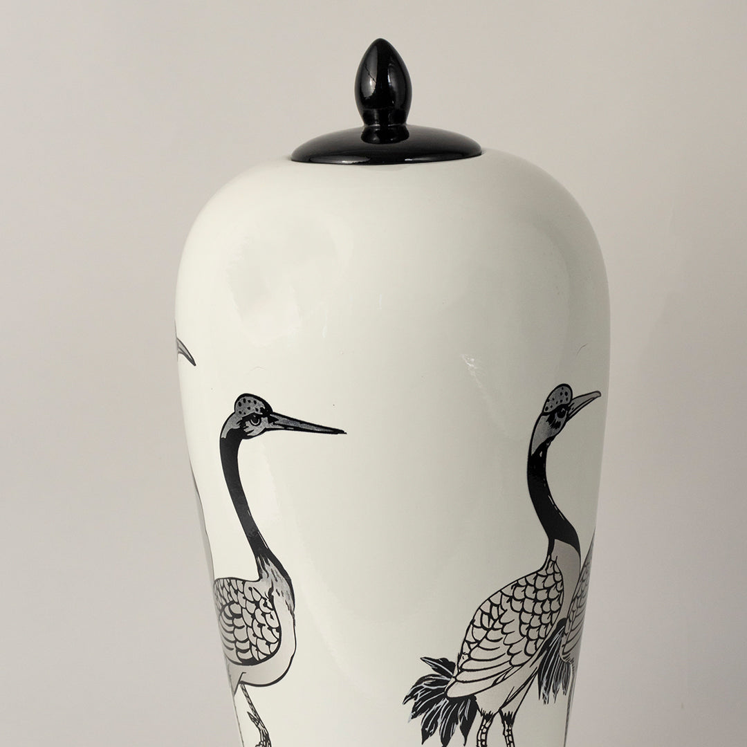White ceramic jar with crane bird illustration and black lid placed on white surface against neutral background highlighting minimal artistic home decor aesthetic.