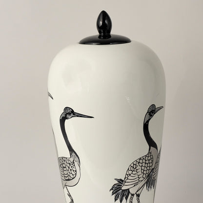 White ceramic jar with crane bird illustration and black lid placed on white surface against neutral background highlighting minimal artistic home decor aesthetic.