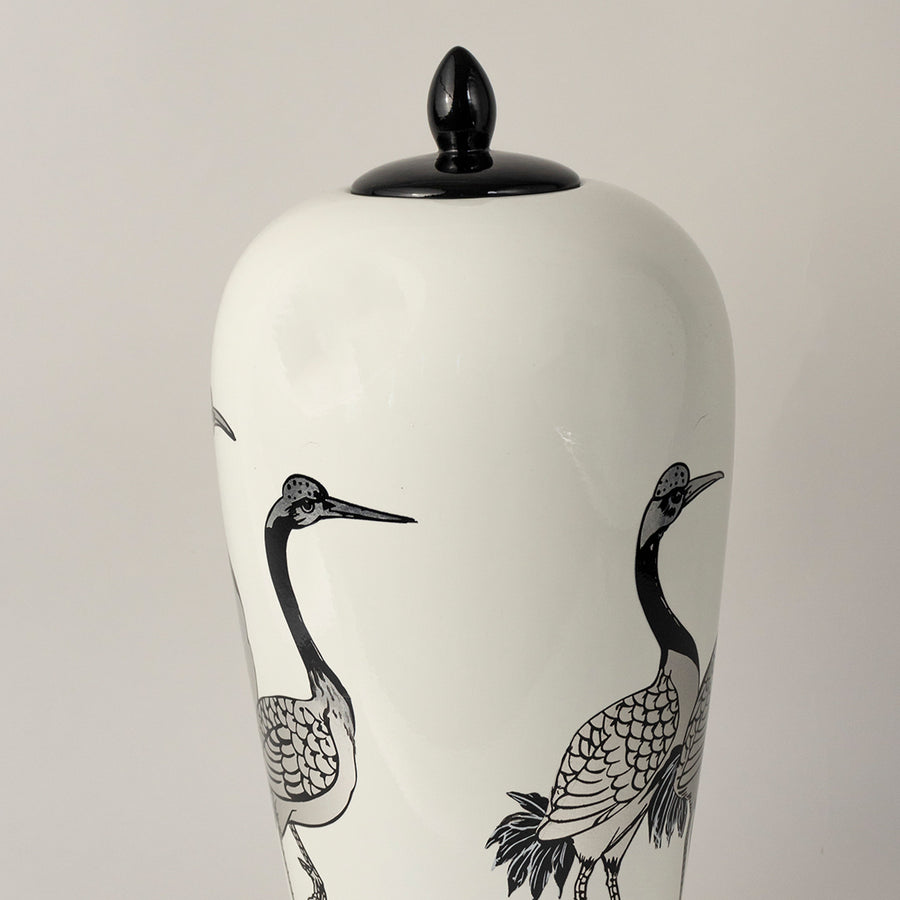 White ceramic jar with crane bird illustration and black lid placed on white surface against neutral background highlighting minimal artistic home decor aesthetic.