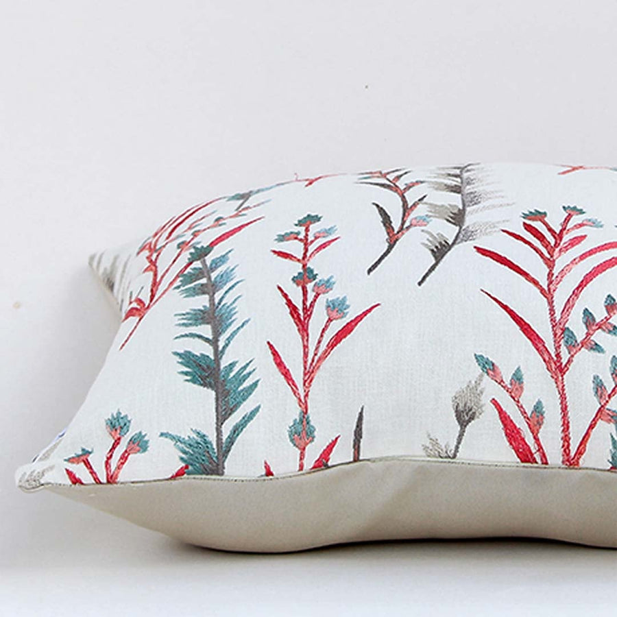 Closeup view of decorative cushion showcasing detailed red and teal botanical print on soft light off white fabric with smooth stitched edges and plush filling visible from the side.