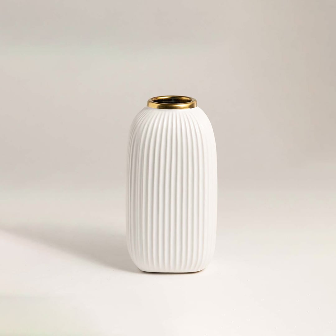Luxurious white ceramic vase with ribbed surface and metallic gold rim placed on a white background under soft lighting.