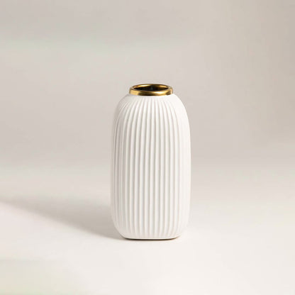 Luxurious white ceramic vase with ribbed surface and metallic gold rim placed on a white background under soft lighting.