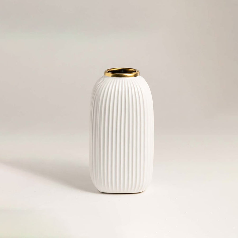 Luxurious white ceramic vase with ribbed surface and metallic gold rim placed on a white background under soft lighting.