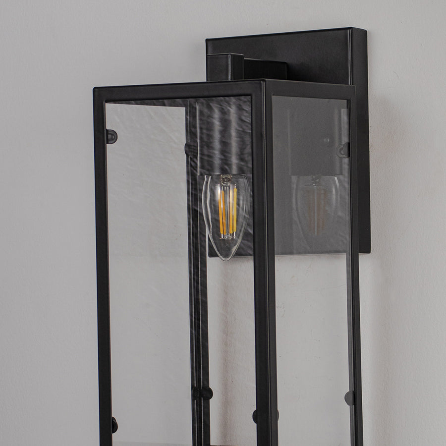 Close up wall light with black metal frame and clear glass panels on neutral background modern exterior lighting fixture.