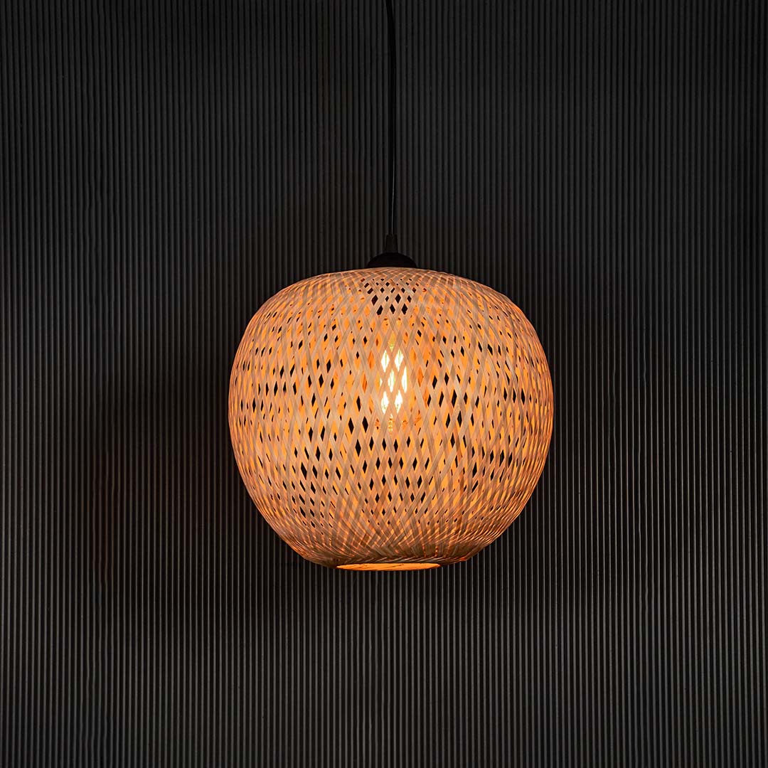 Round rattan pendant light with handwoven bamboo shade turned on glowing softly against plain black background.