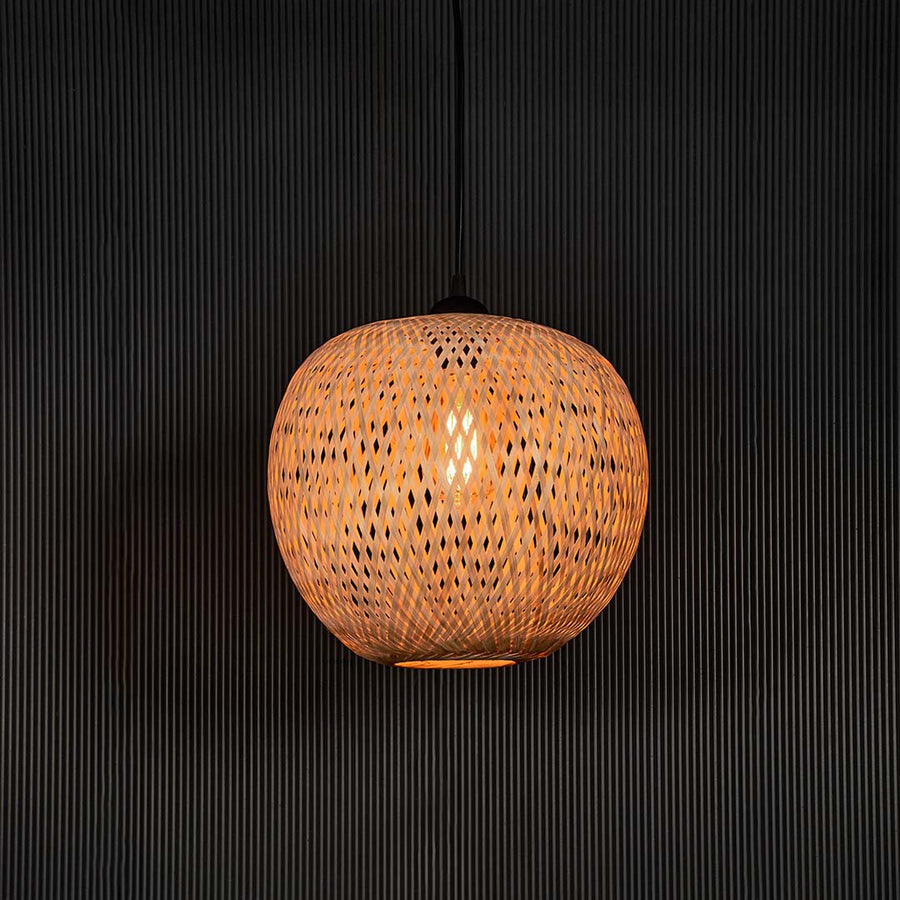 Round rattan pendant light with handwoven bamboo shade turned on glowing softly against plain black background.