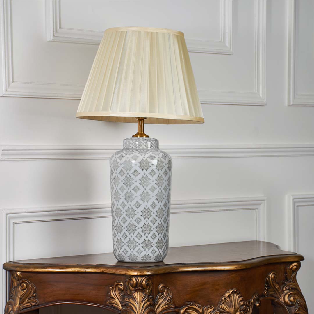 Ceramic table lamp with grey patterned base and pleated cream shade displayed against a simple white background without illumination.