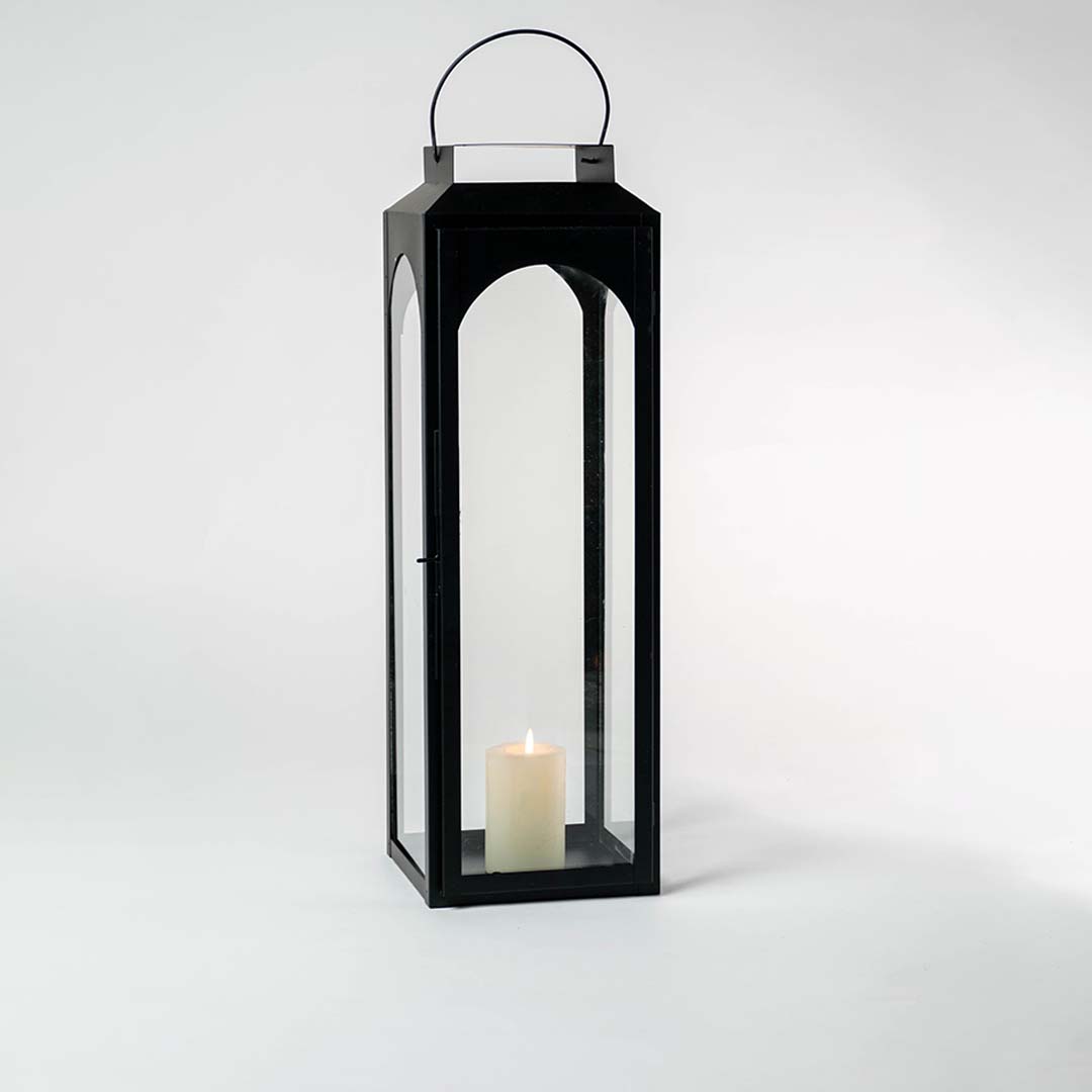 Tall black lantern illuminated softly against a white background showcasing reflective glass and metal sheen.