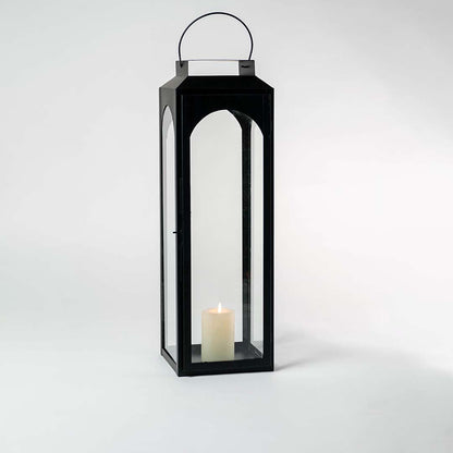 Tall black lantern illuminated softly against a white background showcasing reflective glass and metal sheen.
