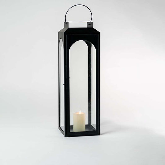 Tall black lantern illuminated softly against a white background showcasing reflective glass and metal sheen.