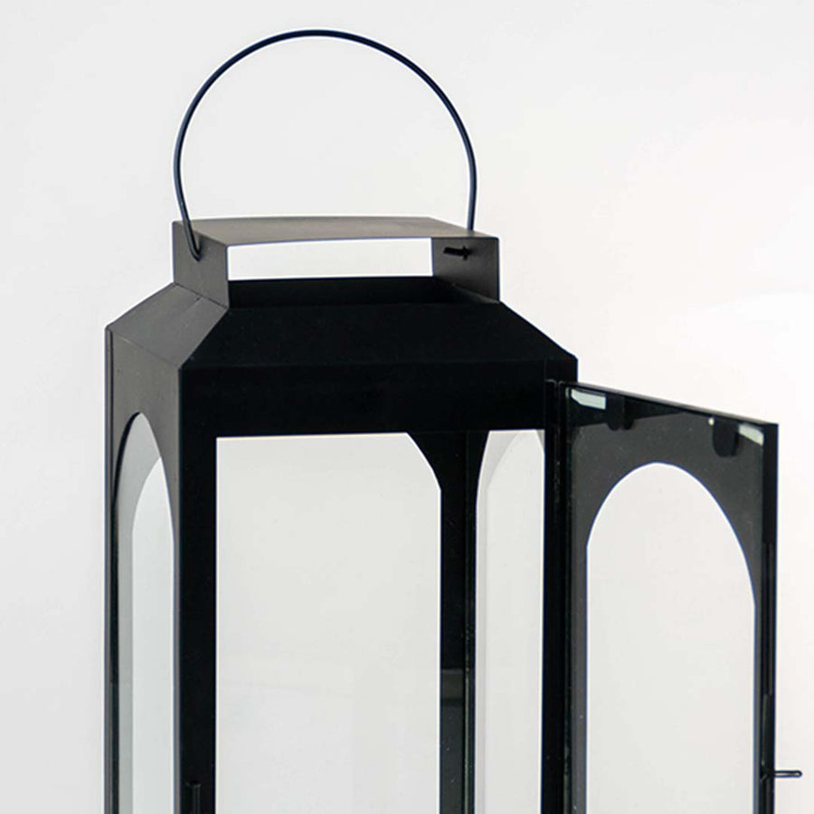 Closeup of black metal lantern with hanging handle and glass panels for modern decor styling use.