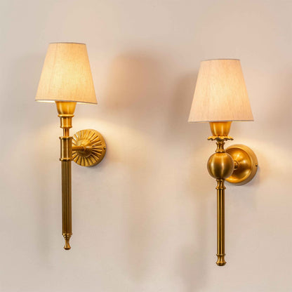 Pair of elegant traditional gold metal torch wall sconces with fabric shades casting warm light onto a plain wall.