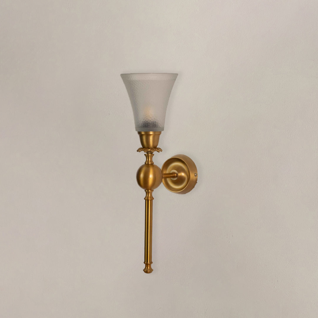 Closeup of gold metal wall light with glass shade on white background suitable for bedside hallway and interior decor.