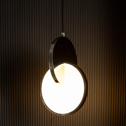 Luna disc pendant light turned on with warm illumination highlighting sleek round metal and frosted glass design against dark backdrop.
