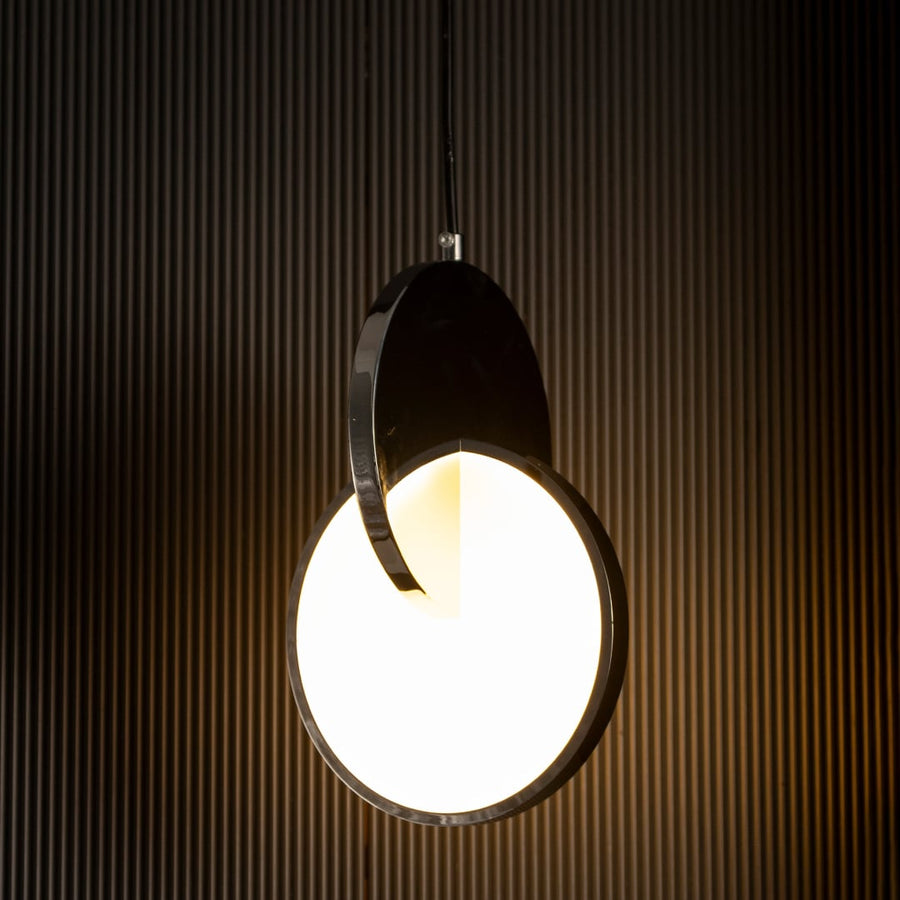 Luna disc pendant light turned on with warm illumination highlighting sleek round metal and frosted glass design against dark backdrop.