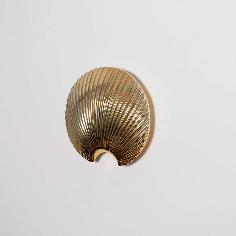 A gold shell design decor accent displayed on a smooth white backdrop showing its refined texture and curved shape with a bright clean aesthetic.