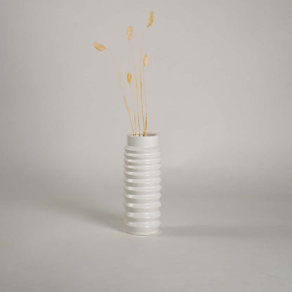 White ceramic vase with ribbed design styled with dried stems adding elegance to minimal modern home decor.