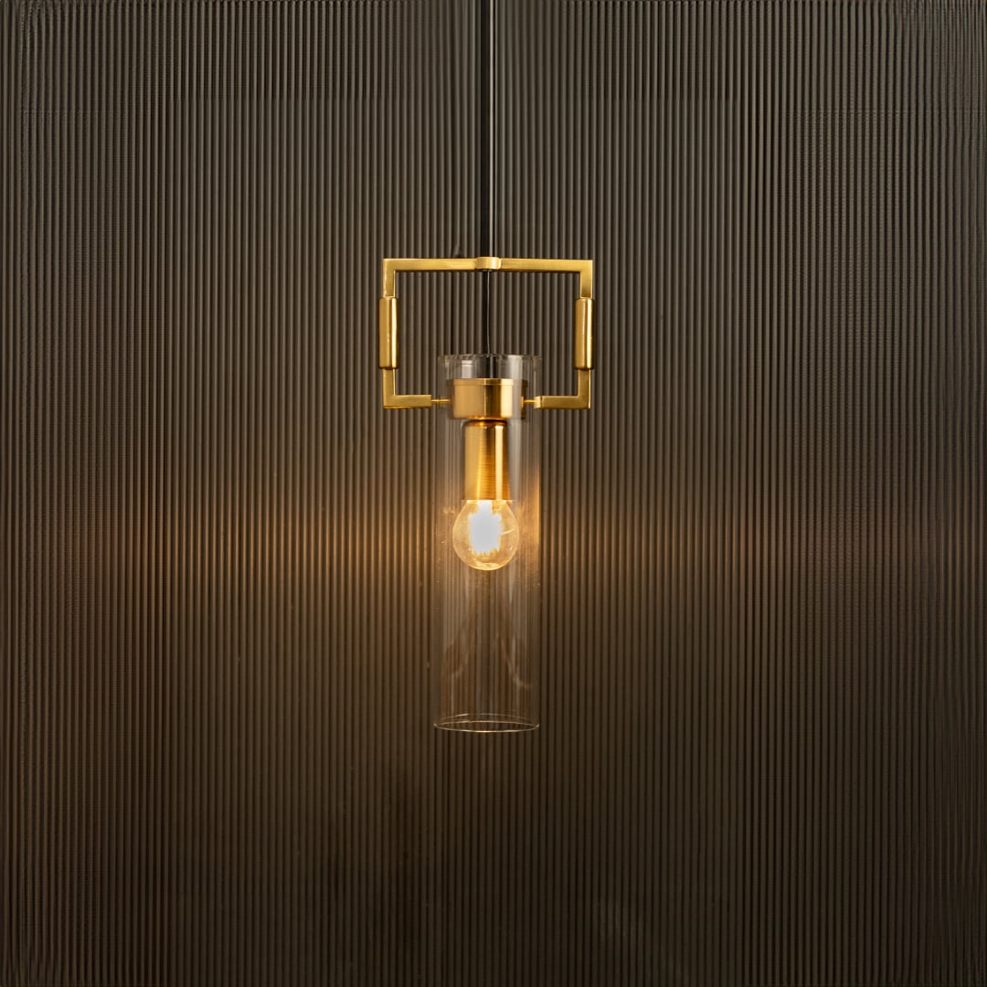 Modern pendant light with clear glass cylinder and gold frame glowing warmly against a textured black background.