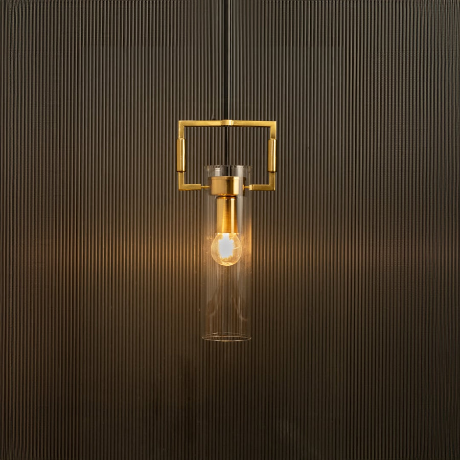 Modern pendant light with clear glass cylinder and gold frame glowing warmly against a textured black background.