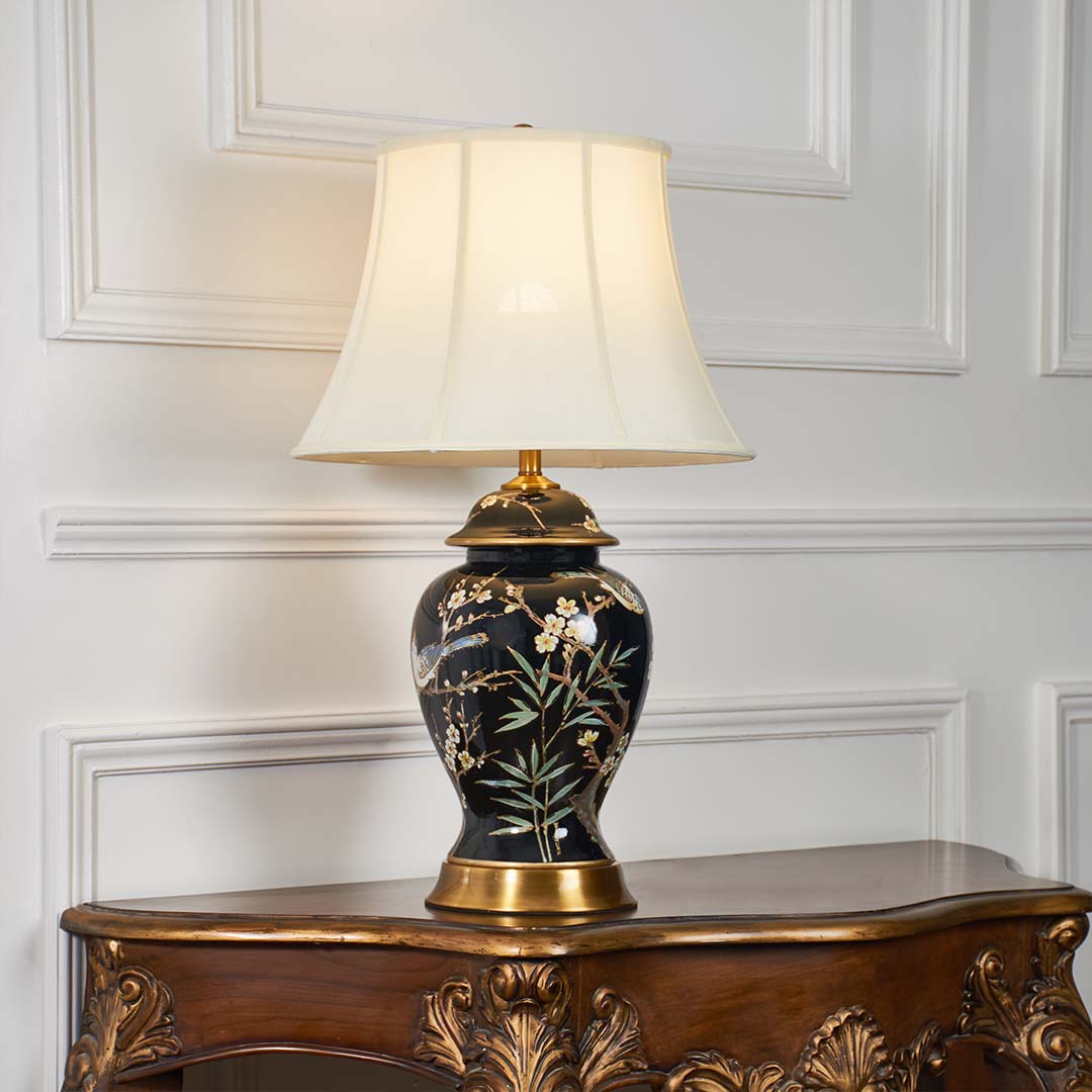 Black floral ceramic table lamp with fabric shade displayed on a carved wooden console table creating elegant ambient lighting.