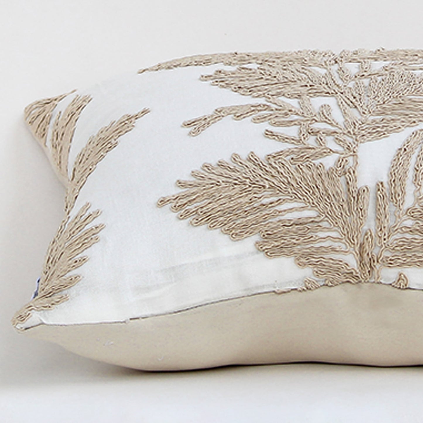 Soft cotton cushion cover with beige floral embroidery displayed at an angle providing an elegant nature inspired décor accent with a breathable gentle and skin friendly material finish.