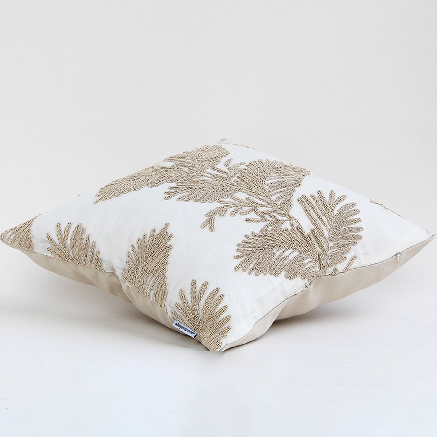 Soft cotton cushion cover with beige floral embroidery shown at an angle providing an elegant nature inspired décor element with a breathable smooth and skin friendly fabric texture.