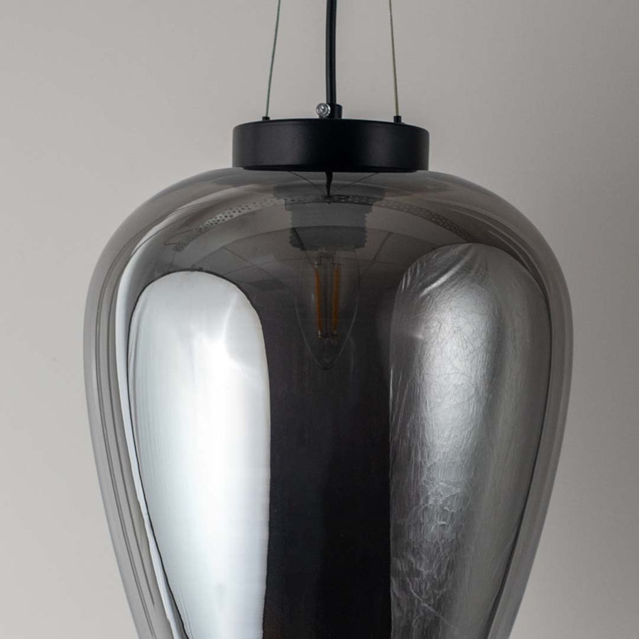 Closeup of smoked glass pendant light with black suspension showing reflective surface and elegant curved shade design.