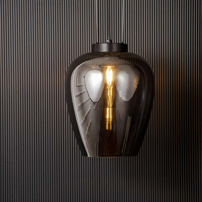 Smoked glass pendant light glowing warmly with filament bulb and black suspension shown on black background for interiors.