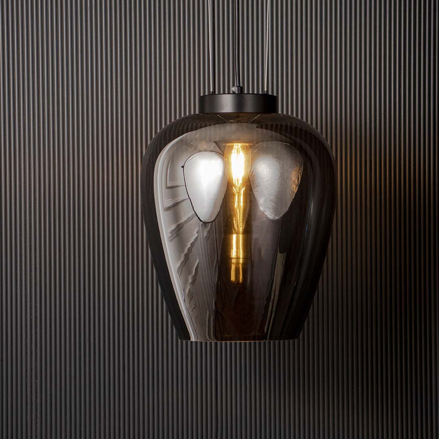 Smoked glass pendant light glowing warmly with filament bulb and black suspension shown on black background for interiors.