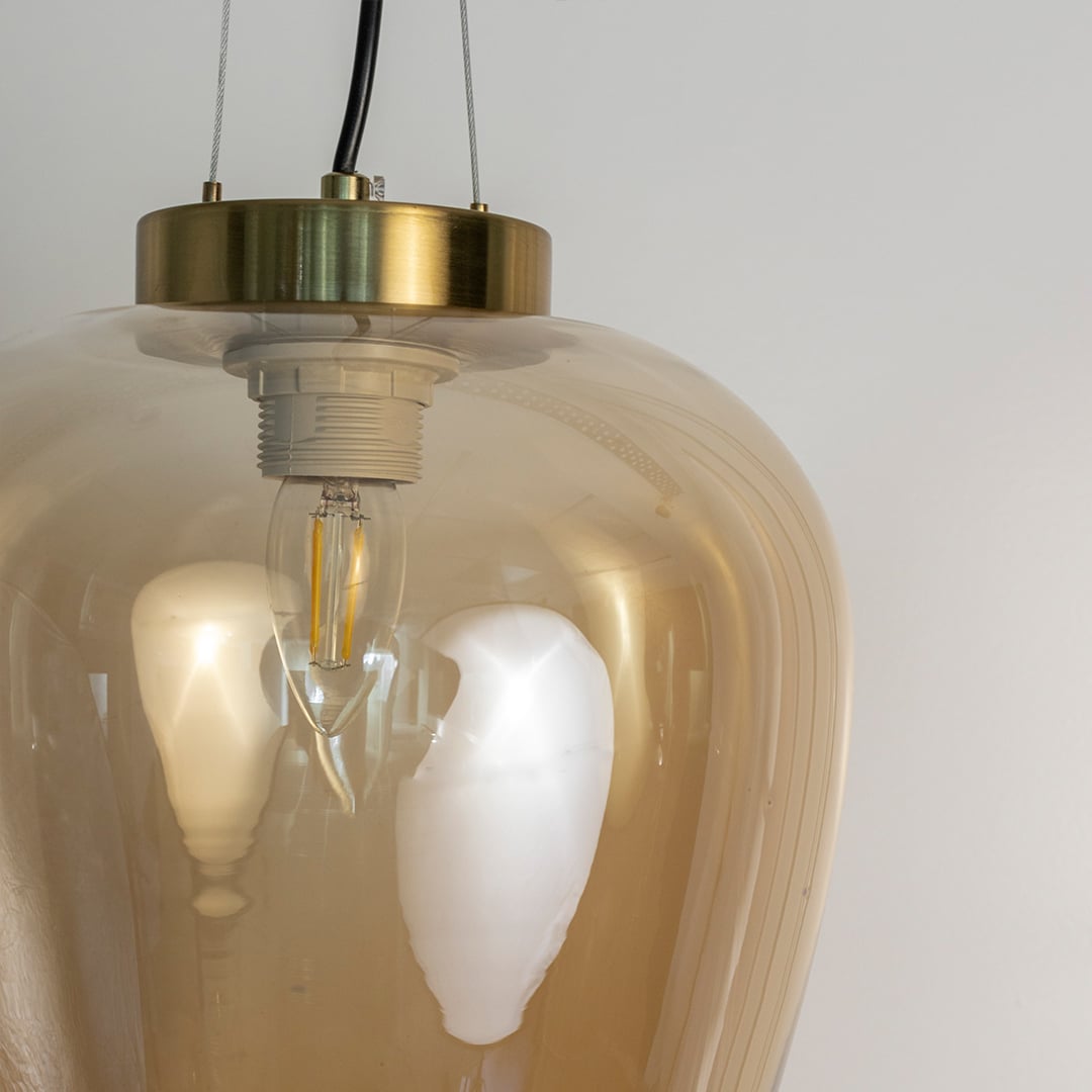 Closeup of amber glass pendant light showing polished brass fixture and curved glass shade with warm reflection.