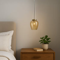 Amber glass pendant light with gold accents beside bedside table adding warmth and modern sophistication.