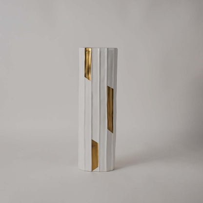 Matte white faceted ceramic cylinder vase accented with polished gold geometric inlays on white background for chic decor.