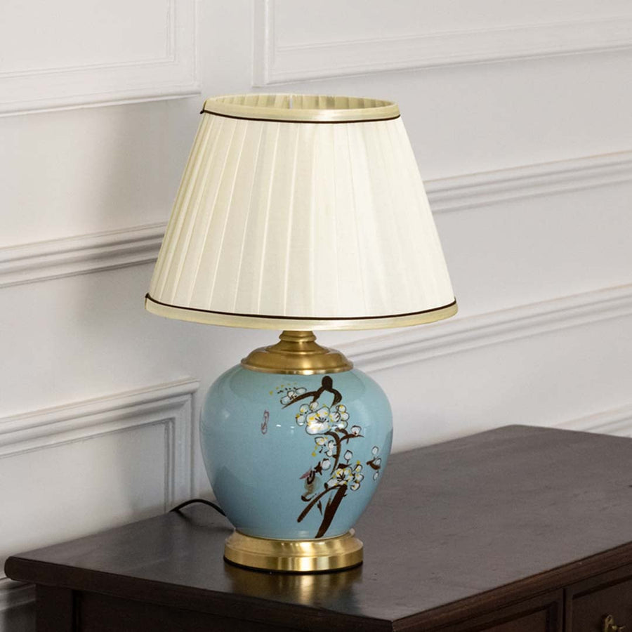 Table lamp with blue ceramic base and white pleated shade presented on a soft white background for clean product detail.