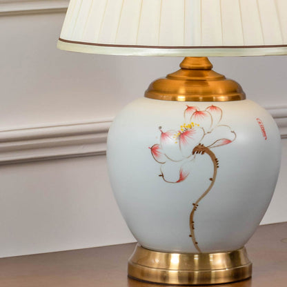Closeup of ceramic table lamp with floral hand painted base golden detailing and fabric shade turned on.