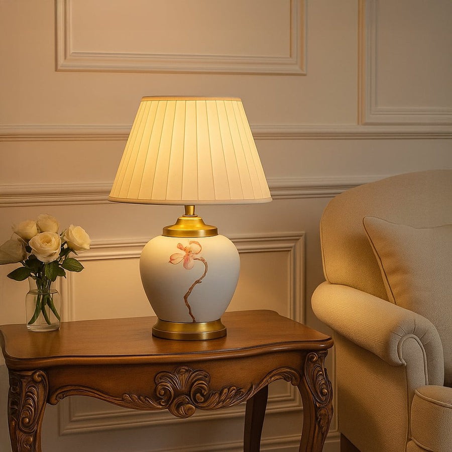 Ceramic table lamp with hand painted floral design and bulb turned on adding warm light to living room decor.