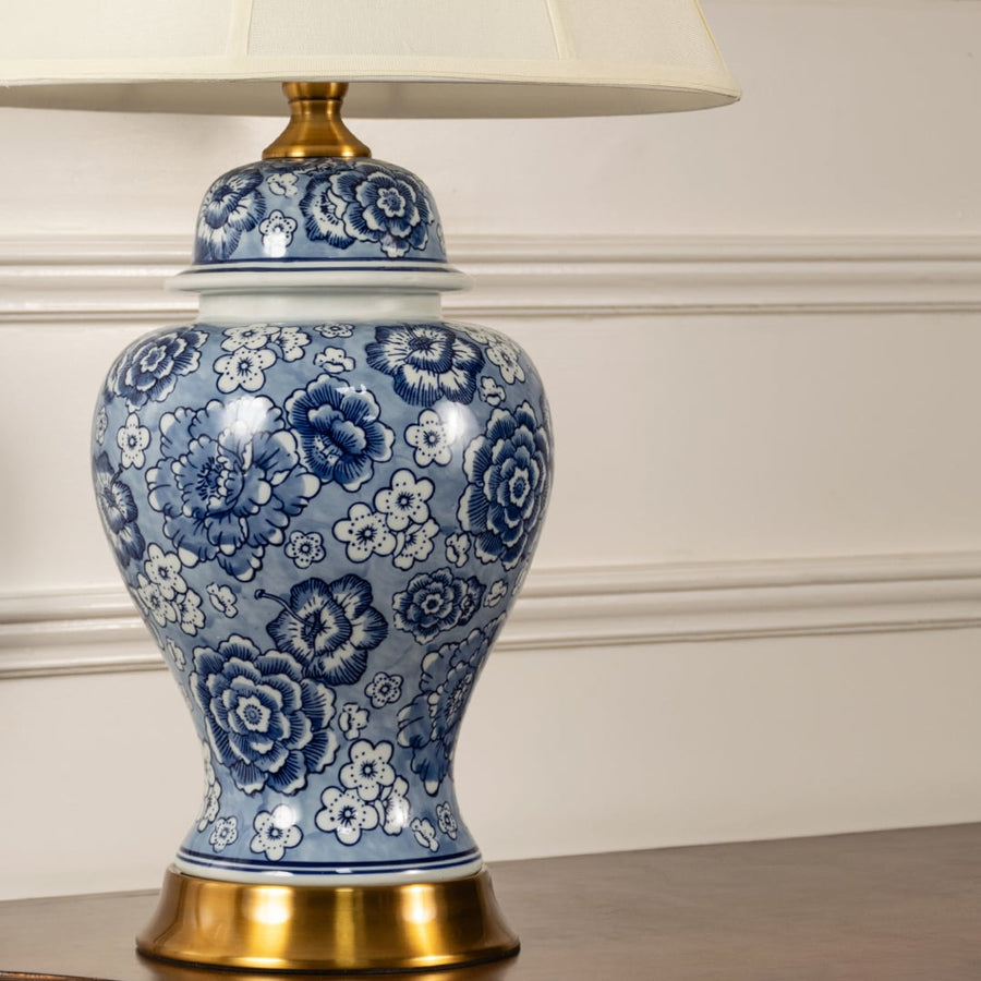 Blue and white ceramic table lamp showcasing intricate floral craftsmanship with brass base and fabric shade design.
