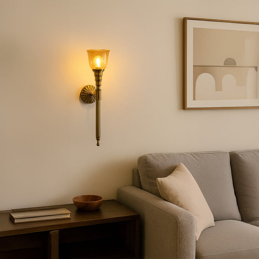 Vintage brass wall sconce with amber glass shade mounted on cream wall creating elegant traditional home lighting decor.