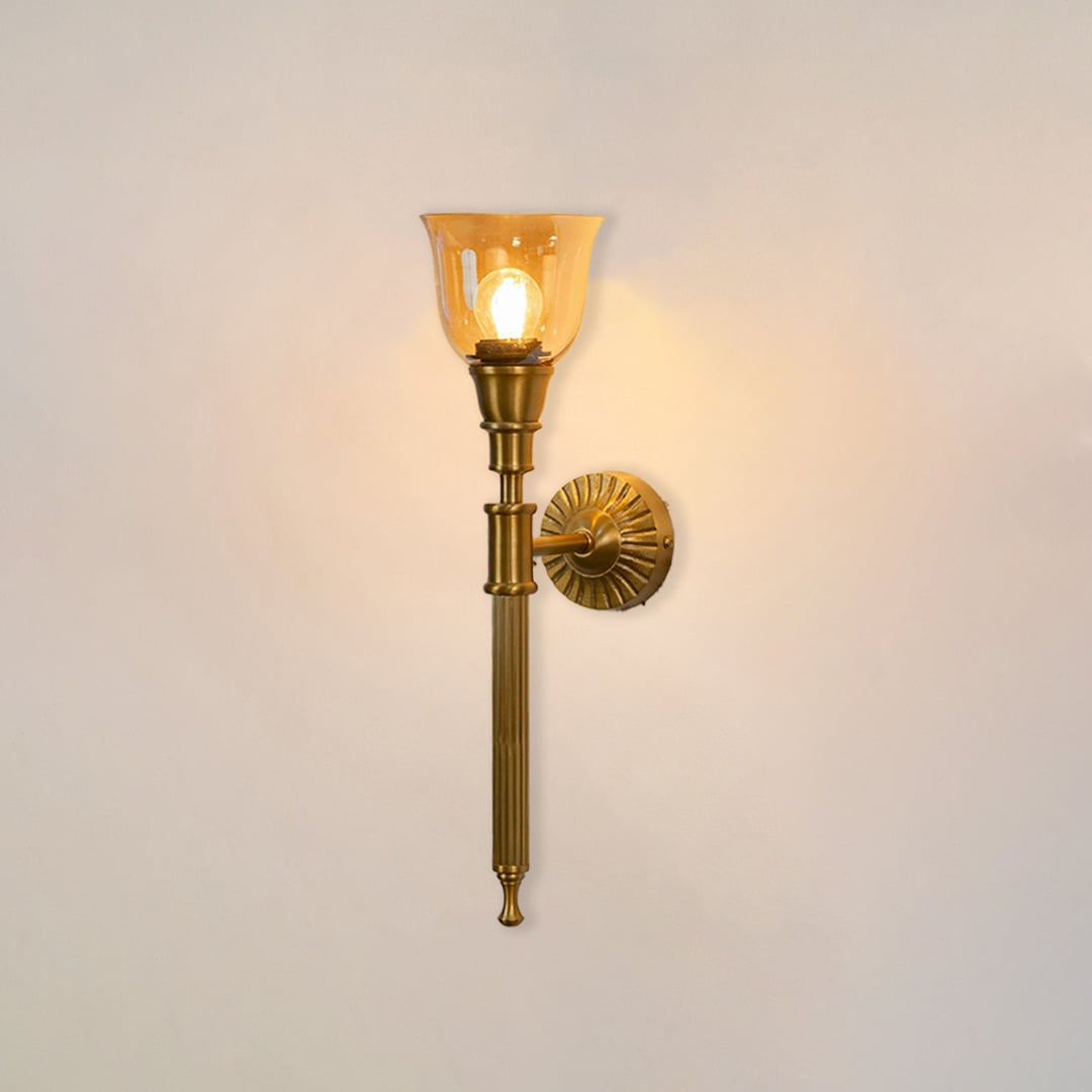 Illuminated antique brass wall lamp with glowing amber glass shade showing warm light on clean white background display.