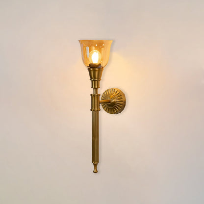 Illuminated antique brass wall lamp with glowing amber glass shade showing warm light on clean white background display.