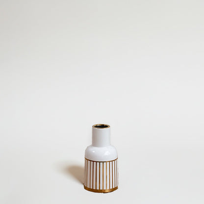 A modern ceramic vase in white with gold striped detailing photographed on a bright background emphasizing its sleek shape and artistic style.