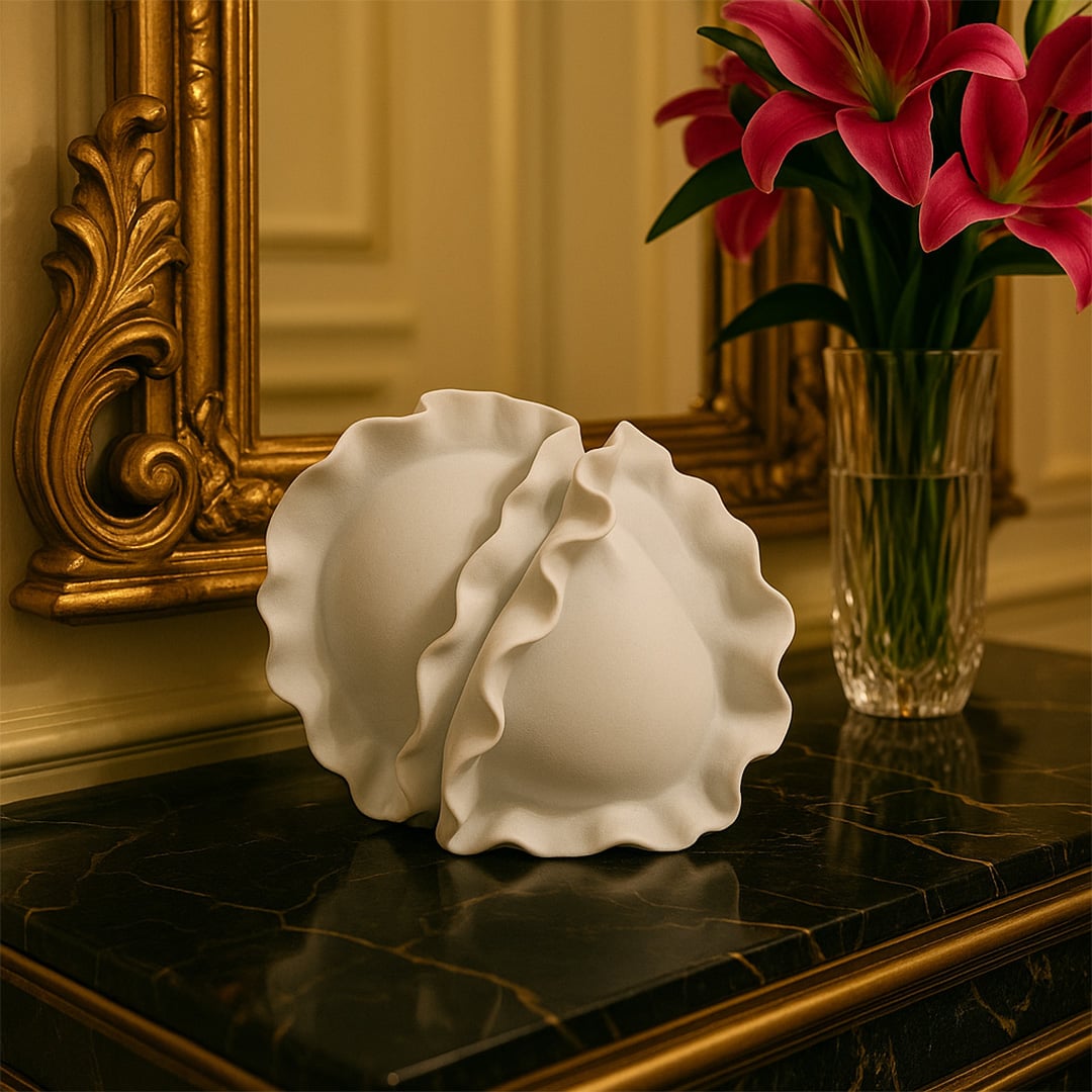 White sculptural ceramic vase featuring dual wave-edged forms placed on a marble tabletop beside a golden ornate mirror.
