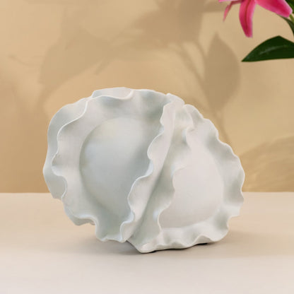 Abstract white sculptural ceramic vase with fluid overlapping design and sculpted wavy edges for modern spaces against white background.