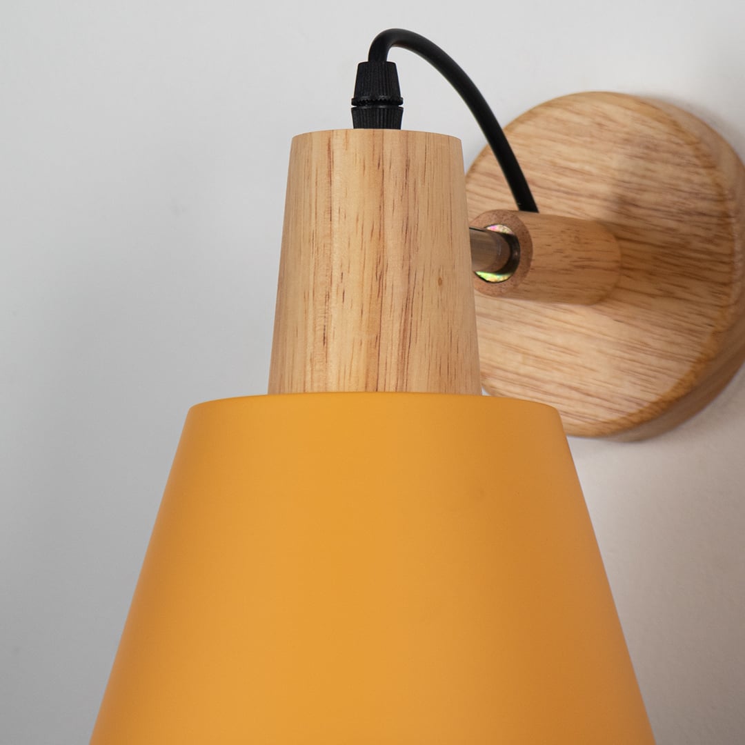Closeup of modern wall lamp with matte mustard yellow metal shade wooden base and black cord showcasing elegant wall lighting design.