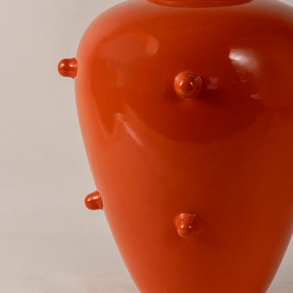 Glossy orange ceramic vase with rounded shape and raised dot texture placed on white surface against neutral background closeup showcasing vibrant decorative appeal.