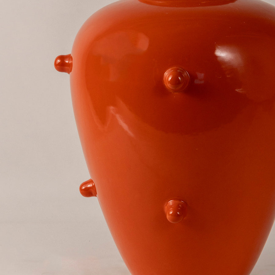 Glossy orange ceramic vase with rounded shape and raised dot texture placed on white surface against neutral background closeup showcasing vibrant decorative appeal.