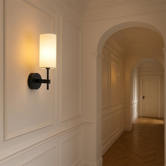 Black metal wall light with tall white fabric shade styled in a modern room setting adding warm ambient lighting for hallways and bedrooms.
