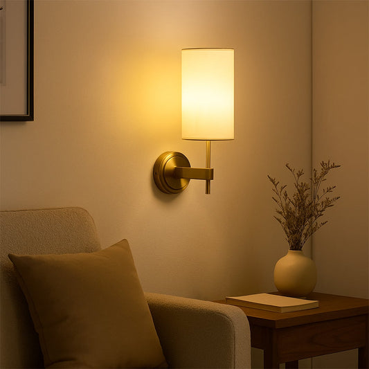 Gold metal wall light with tall white fabric shade styled in a modern room setting creating warm ambient lighting for hallways and bedrooms.