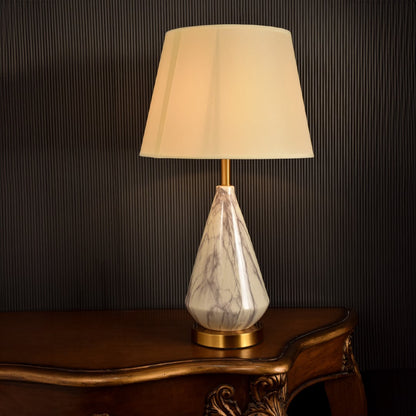 Premium marble and metal table lamp with a glowing beige shade exuding warmth and elegance against a dark backdrop perfect for upscale interiors.