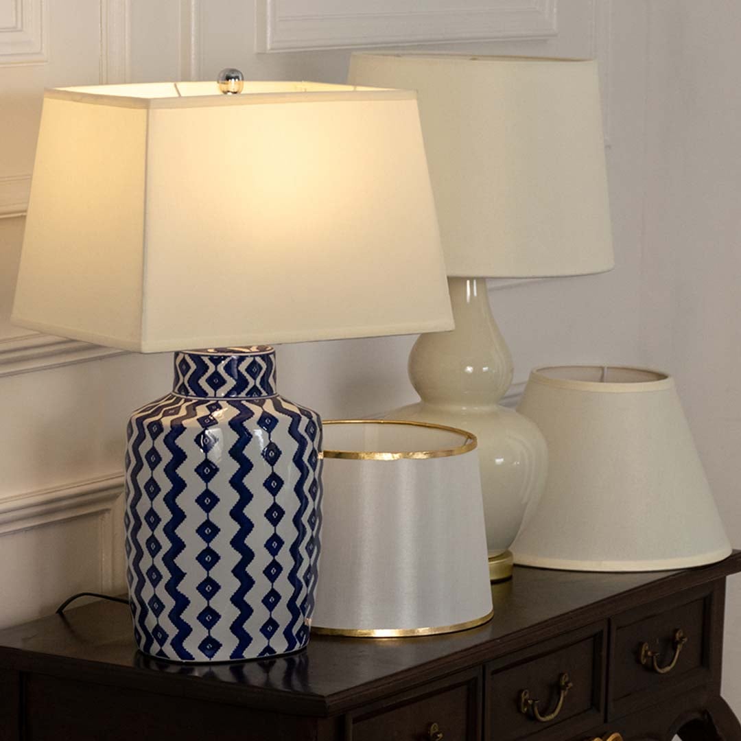 Beige shade blue patterned lamp on console table with light on and cream wall background for soft decorative décor.